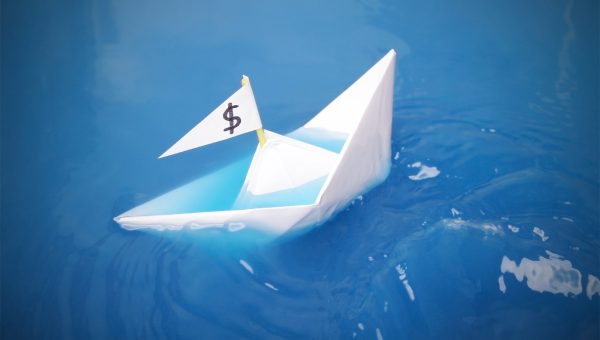 paper boat with a dollar sign on its flag is sinking in blue water